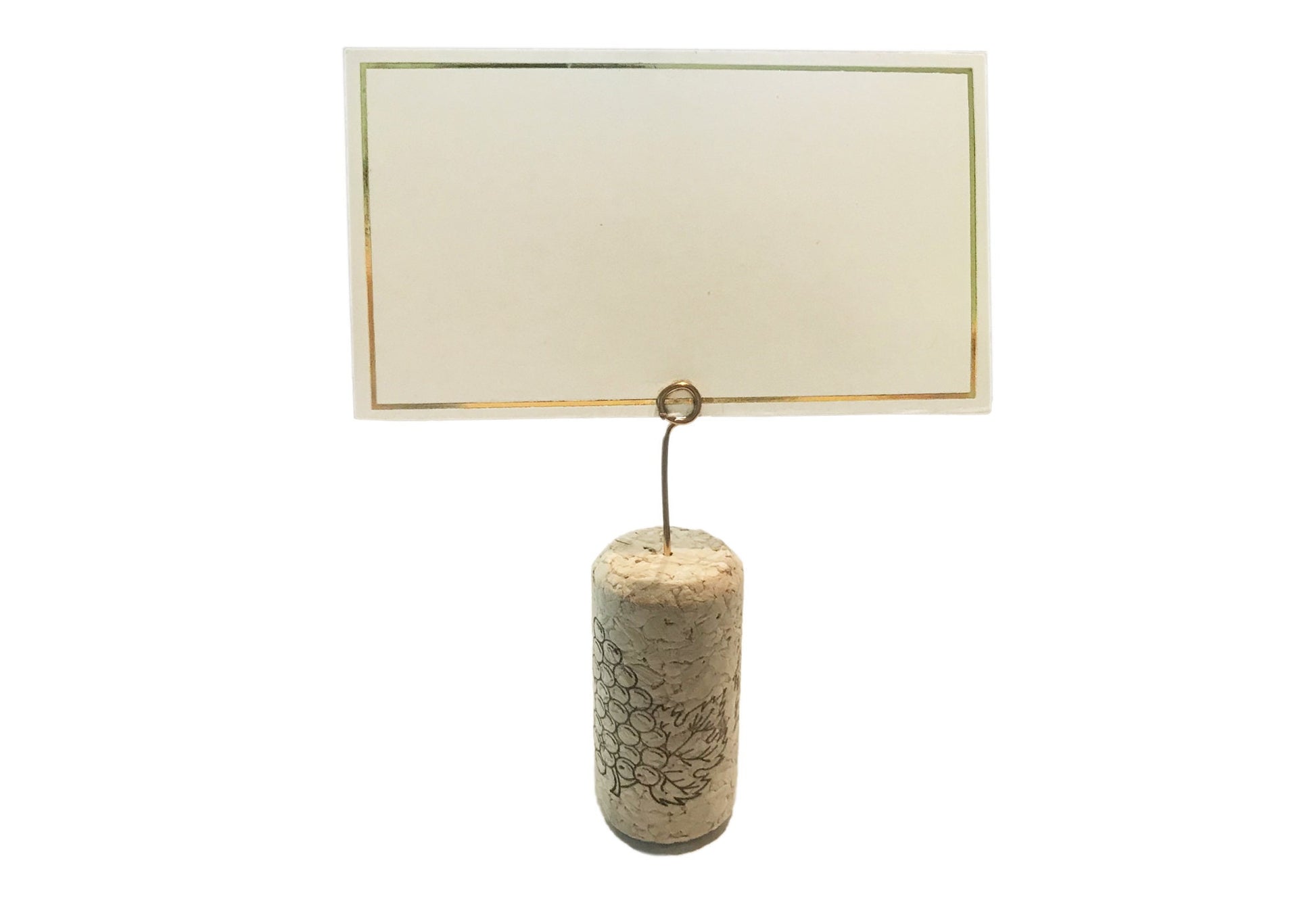 Close-up of mini round gold wire place card clip in a wine cork with a white card inserted.